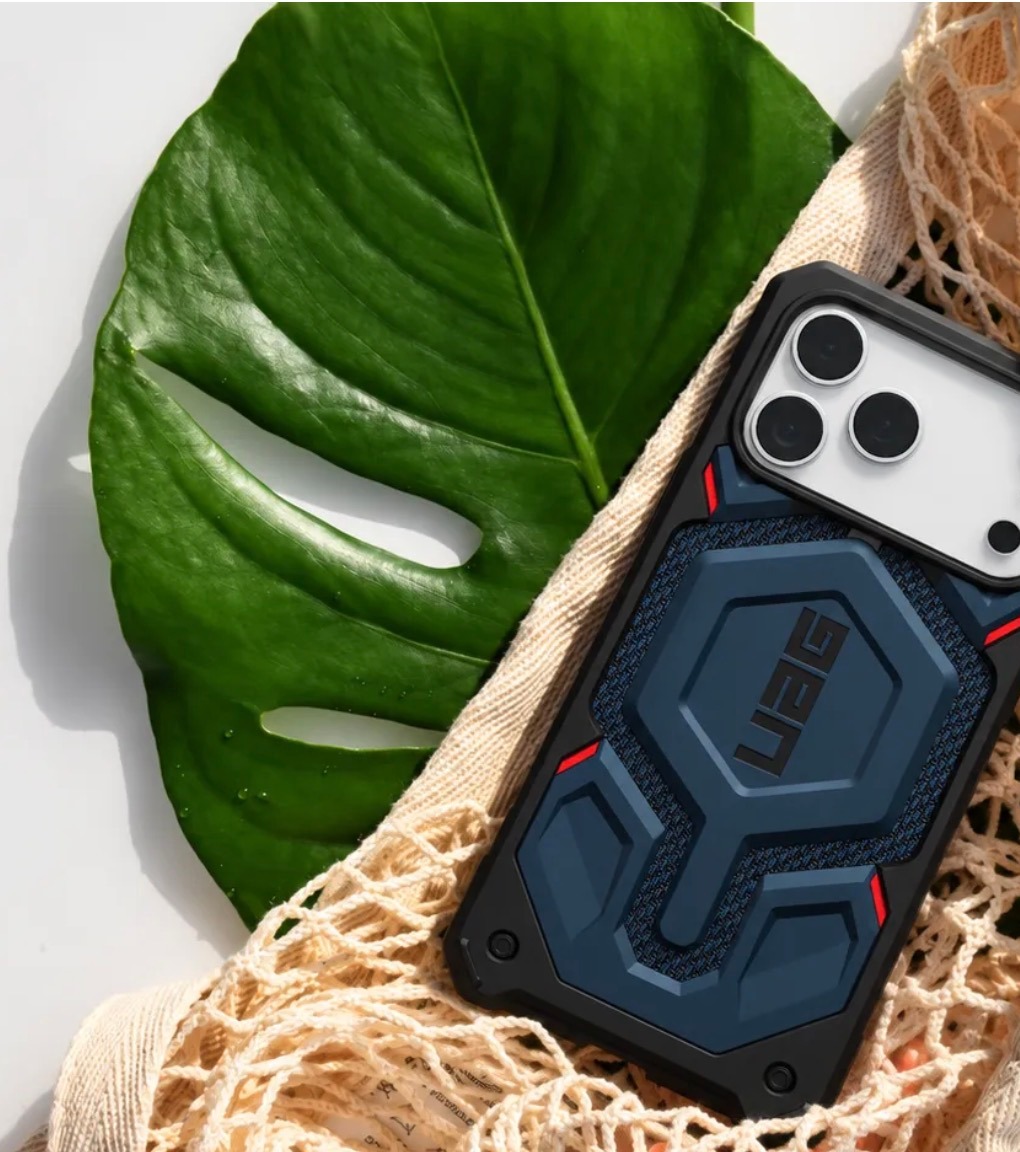 Blue UAG phone case resting in a woven bag beside a green monstera leaf
